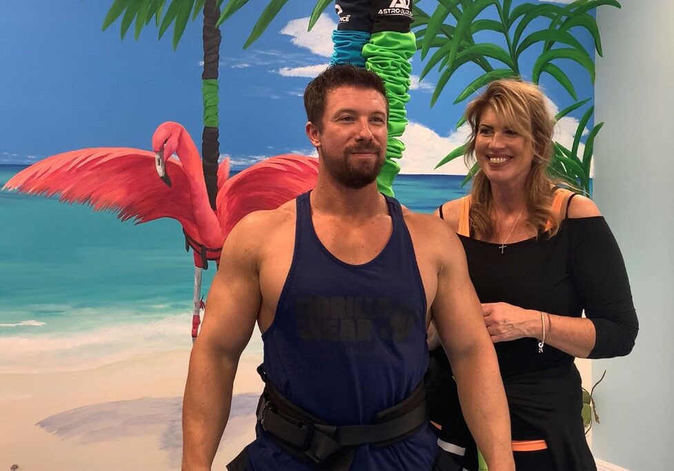 Joyful couple in tropical setting, showcasing fitness and fun with vibrant beach backdrop.